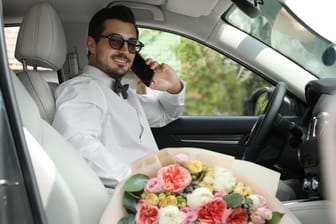 Ein Mann sitzt im Hochzeitsanzug im Auto und telefoniert (Symbolfoto): Im mittelfränkischen Bamberg kann die Trauung samt Erinnerungsfunktion online gebucht werden.