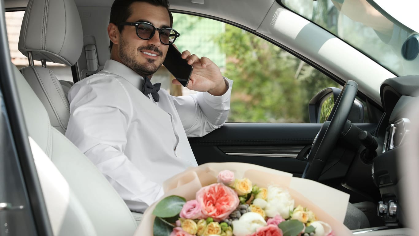 Ein Mann sitzt im Hochzeitsanzug im Auto und telefoniert (Symbolfoto): Im mittelfränkischen Bamberg kann die Trauung samt Erinnerungsfunktion online gebucht werden.