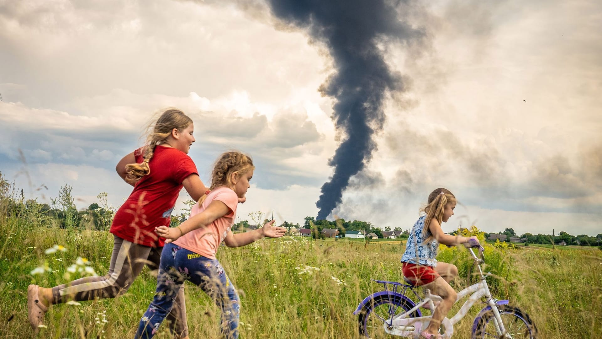 Ukraine: Unter den dunklen Wolken des Krieges übt die fünfjährige Alina, begleitet von Freundinnen, das Fahrradfahren auf einer Wiese im Nordwesten der Ukraine.