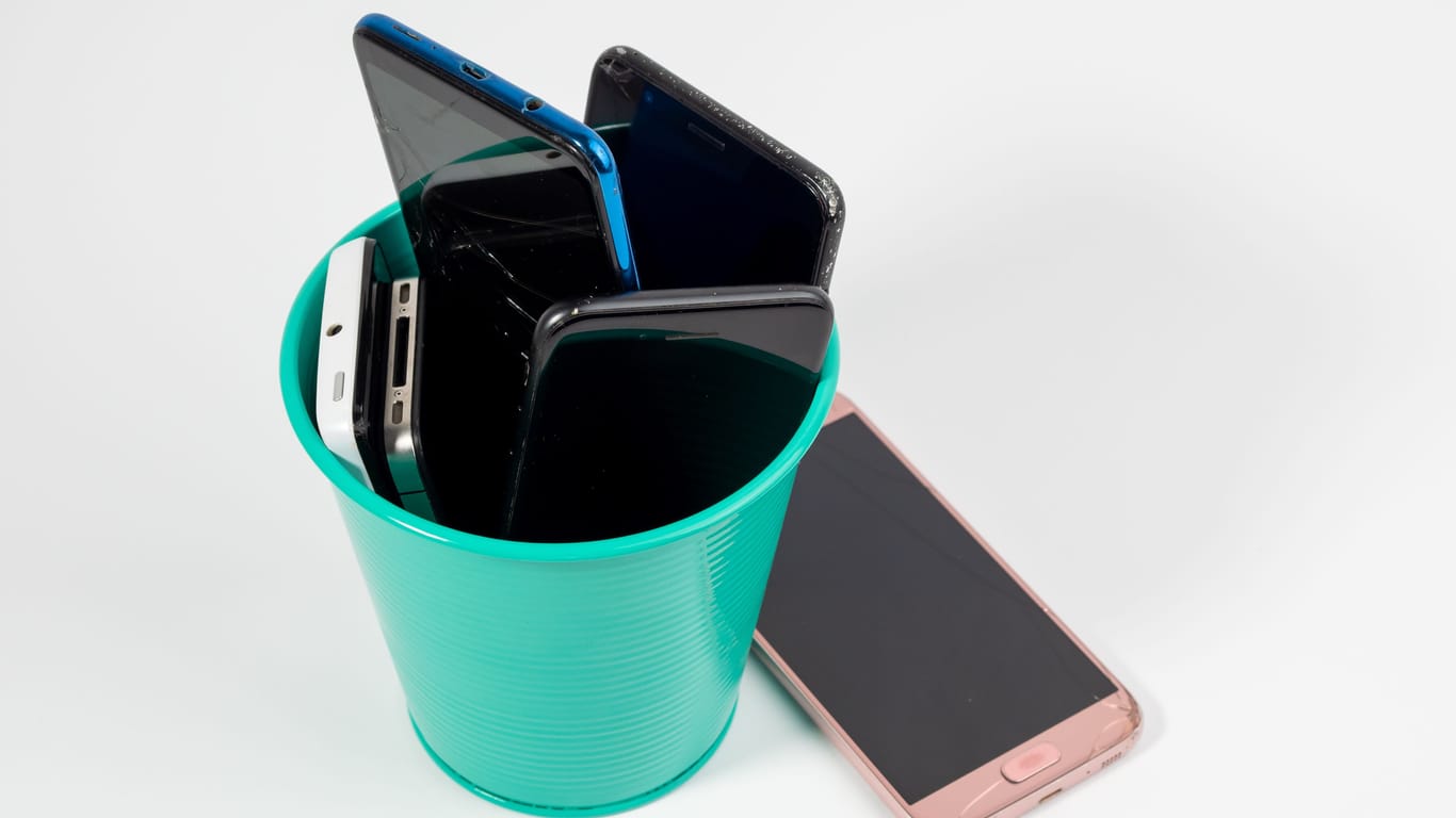 Full trash can of old smartphones on a white background.