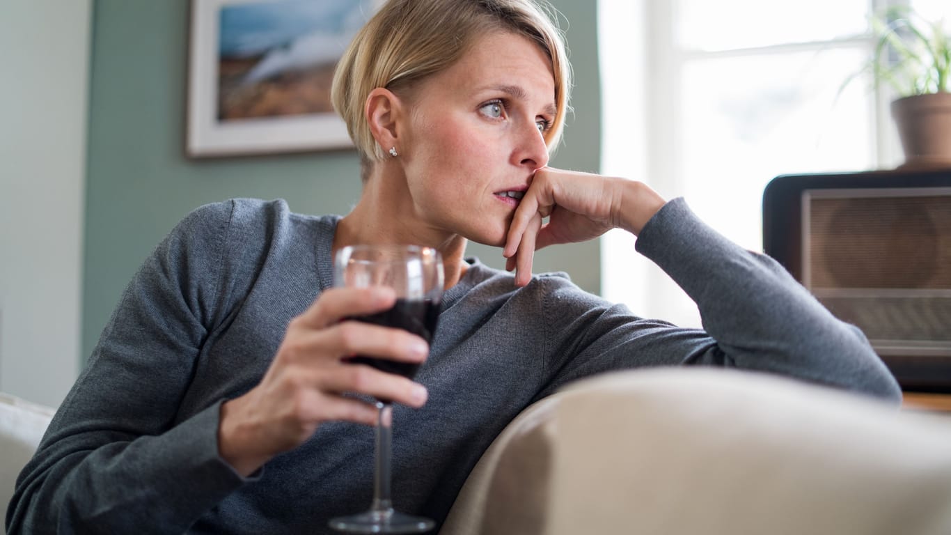 Eine Frau sitzt auf dem Sofa und hält ein Glas Rotwein in der Hand.