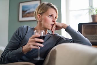 Eine Frau sitzt auf dem Sofa und hält ein Glas Rotwein in der Hand.
