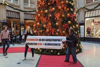 Klimaaktivisten entrollen ein Banner vor dem Weihnachtsbaum in Leipzig: