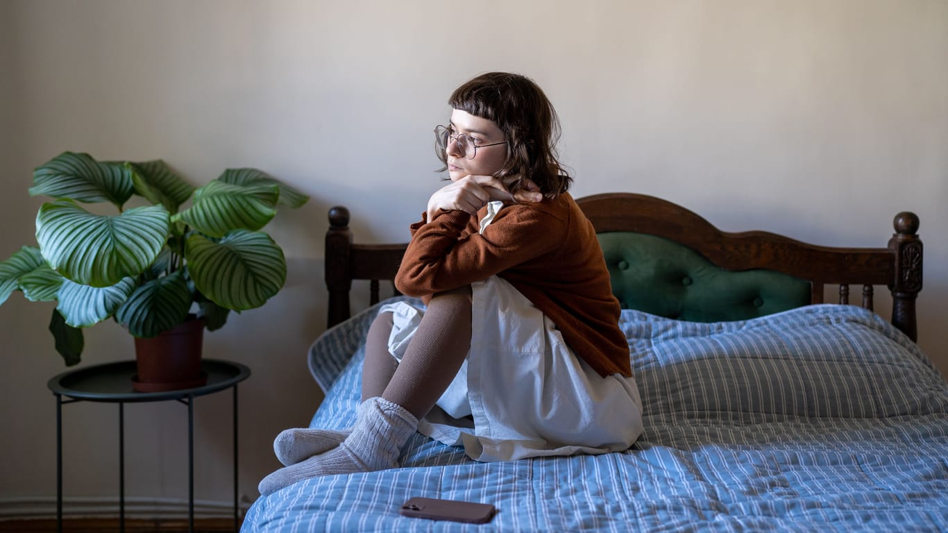 Upset girl teenager sitting on bed at home feeling lonely and isolated