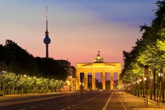Leere Straße des 17. Juni im Morgenrot mit Brandenburger Tor und Berliner Fernsehturm