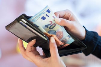 Eine Person nimmt Banknoten aus einem Portemonnaie: 2024 bringt an einigen Stellen Erleichterung, an anderen wird es teurer.