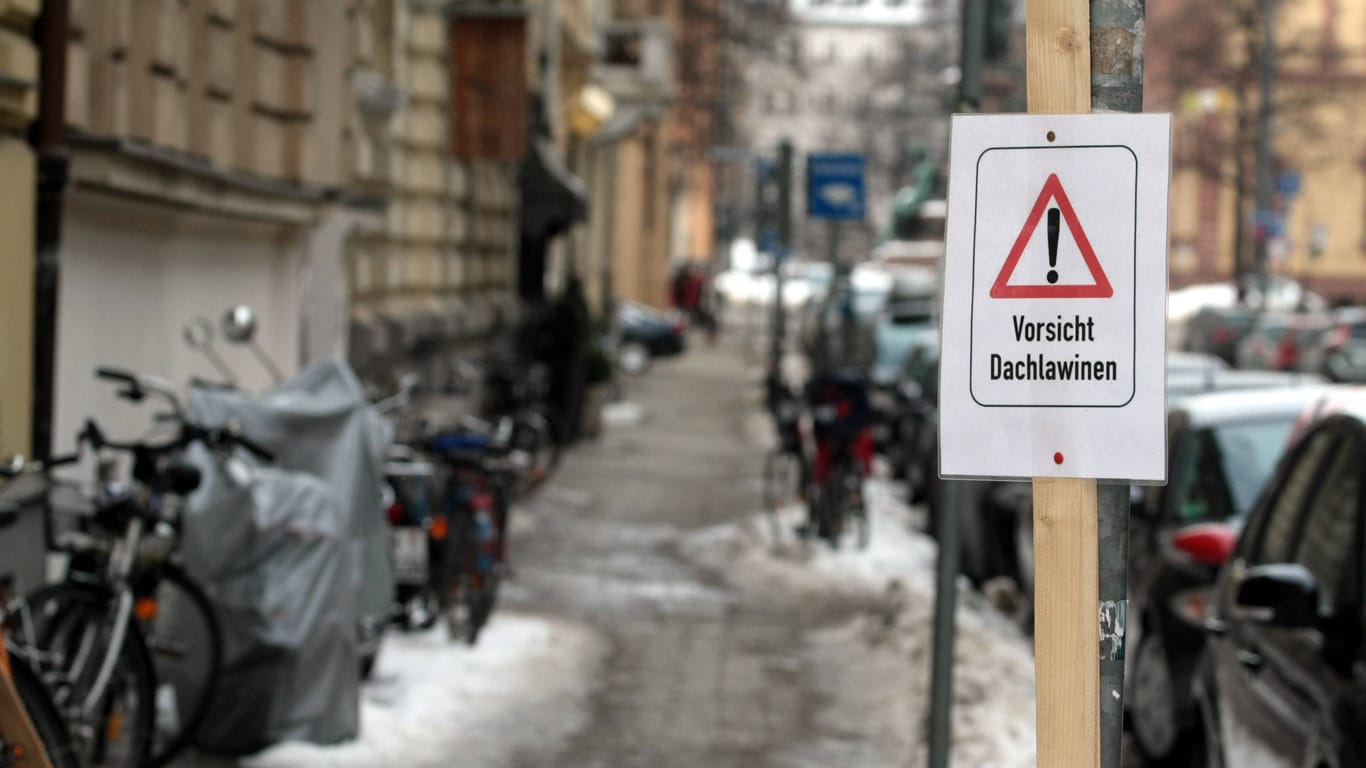 Warnschild mit Aufschrift Vorsicht Dachlawinen auf einem Gehweg vor einer Hausfassade in München (Archivbild).
