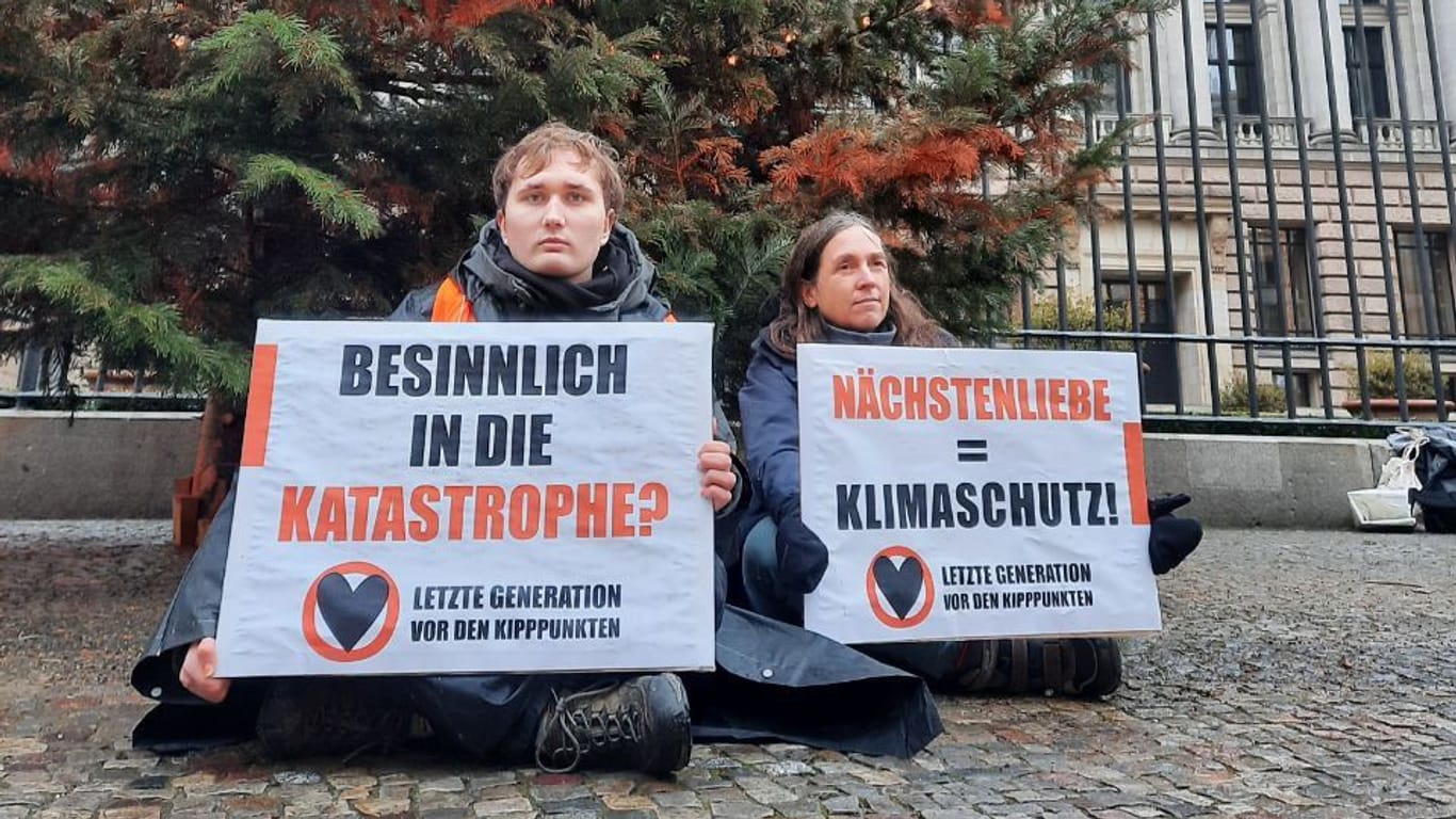 Zwei Aktivisten der "Letzten Generation" sitzen vor einem Weihnachtsbaum in Berlin. Auch in Bayern waren sie aktiv.