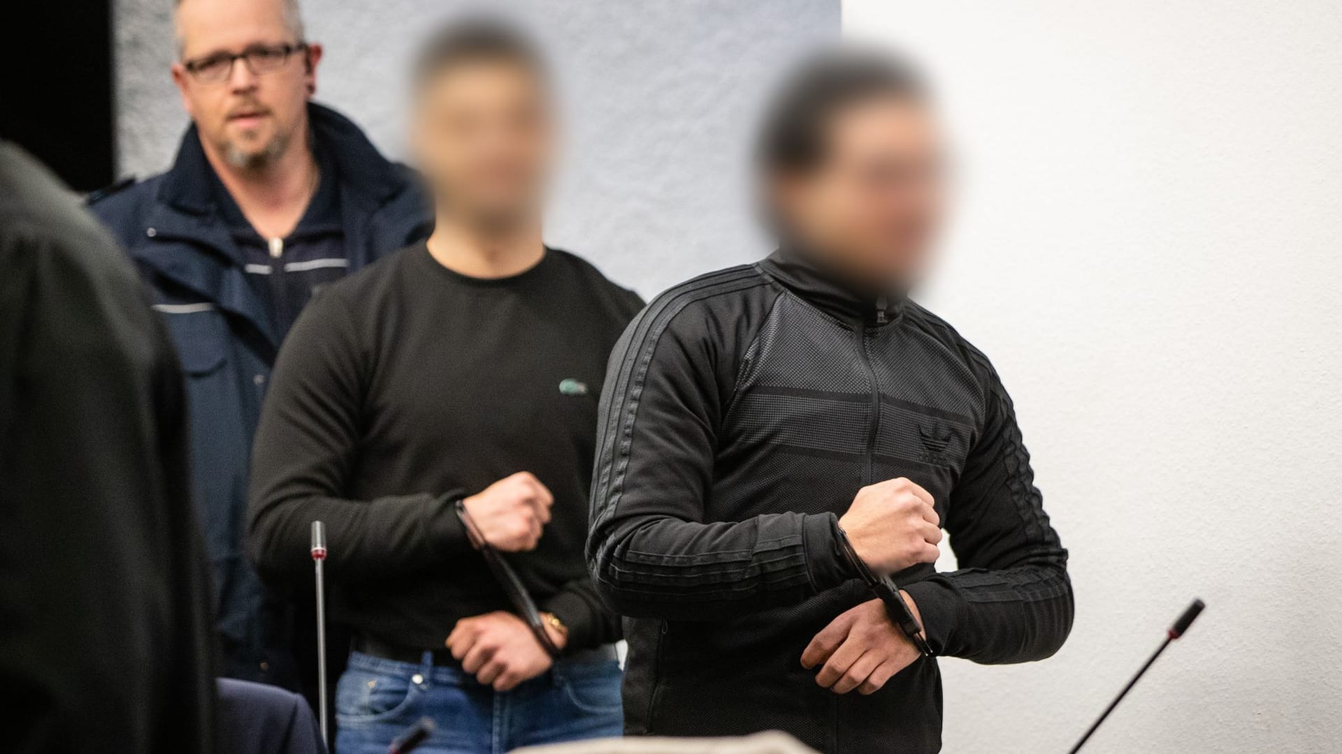 Zwei von fünf Angeklagten werden in einen Gerichtssaal des Landgerichts geführt. Sie sollen einem mutmaßlichen Granatenwerfer verprügelt haben. Zwei von fünf Angeklagten werden in einen Gerichtssaal des Landgerichts geführt. Sie sollen einem mutmaßlichen Granatenwerfer verprügelt haben.