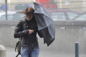 Junge Frau mit Regenschirm im Sturm (Symbolbild): In Hamburg wird das Wetter ungemütlich.