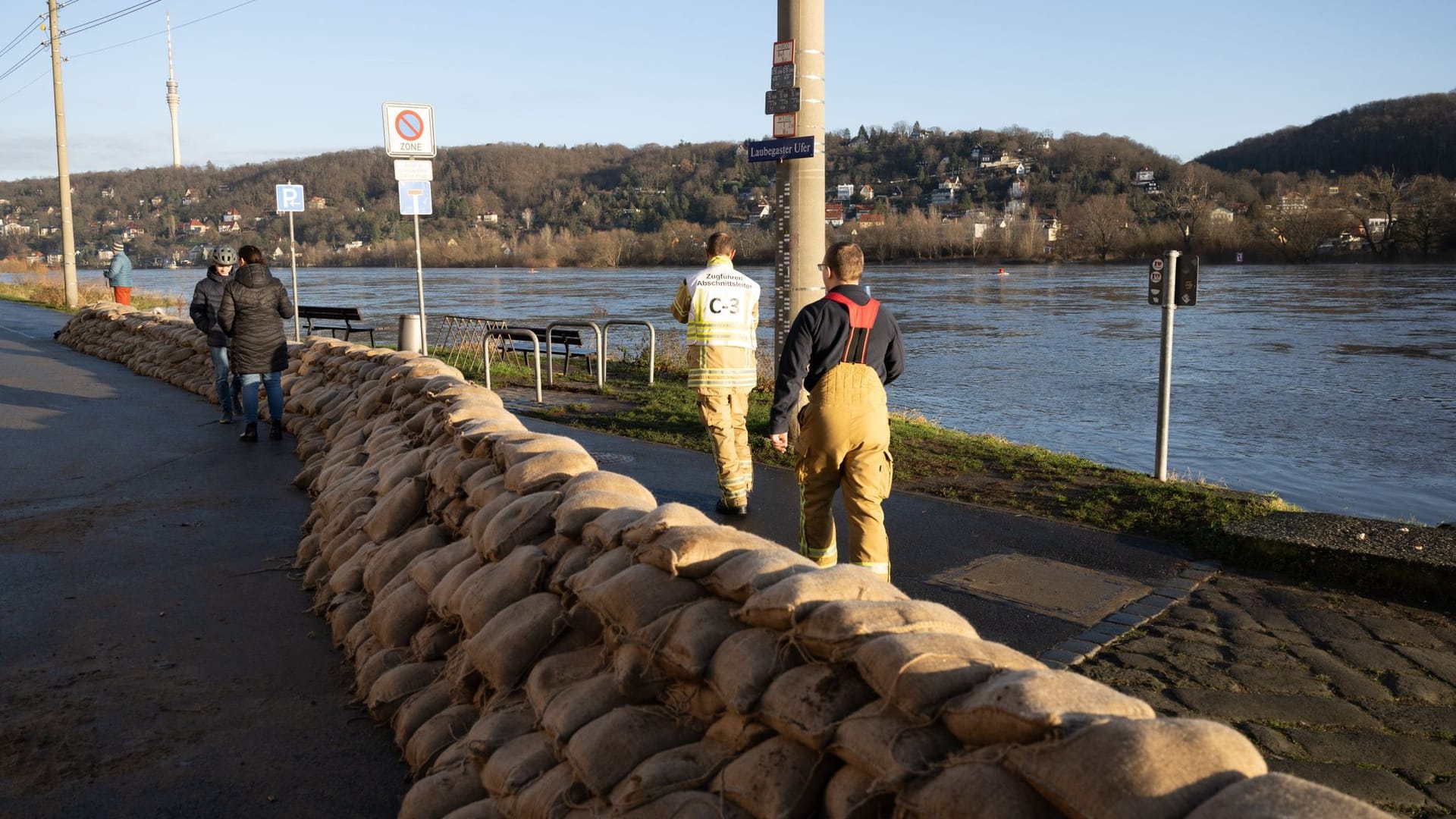 Feuerwehrmänner stehen im Dresdner Stadtteil Laubegast hinter einem Wall aus Sandsäcken am Ufer der Elbe. Das Hochwasser der Elbe in Dresden nähert sich weiter der zweithöchsten Alarmstufe drei.