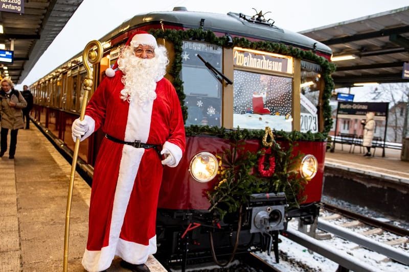 02.12.2023, Berlin: Ein Mann in Weihnachtsmannkostüm steht vor dem Weihnachtszug des Vereins Historische S-Bahn