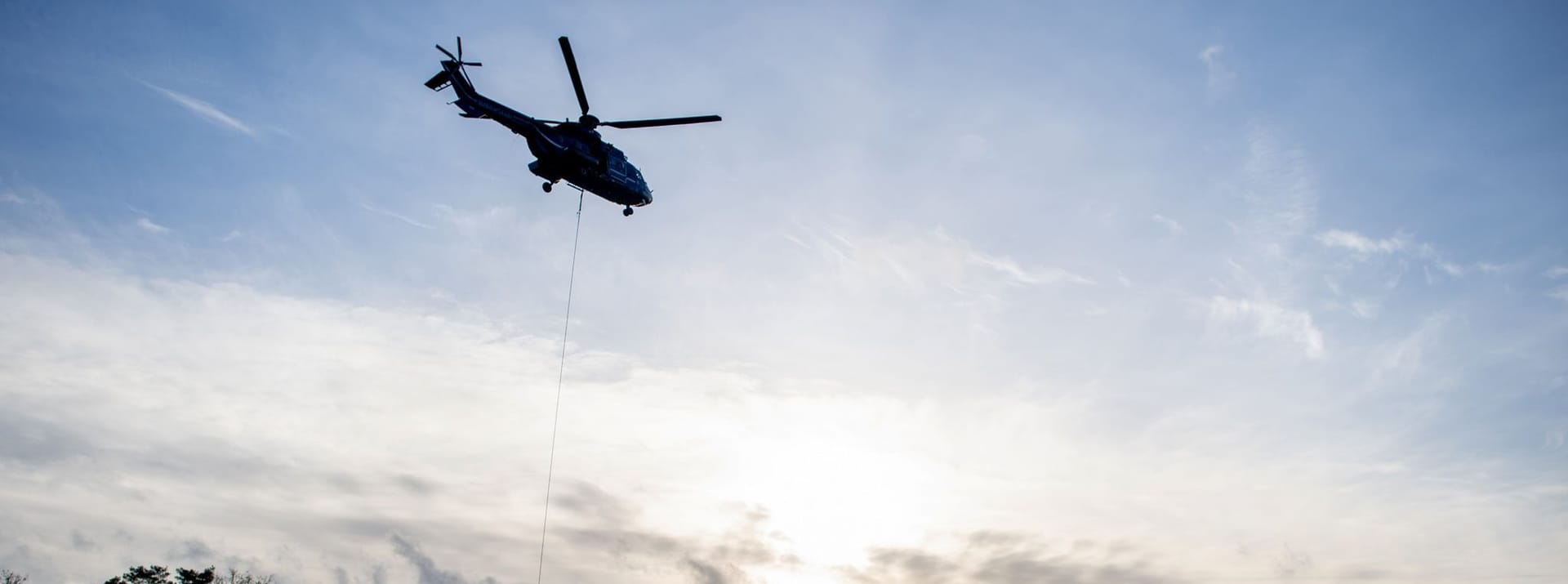 Ein Hubschrauber der Bundespolizei ist in einem Waldgebiet in der Nähe der Hunte in Niedersachsen im Einsatz, um einen Deich mit großen Sandsäcken zu sichern.