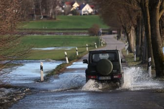 Bayern, Gessertshausen: Ein Auto fährt auf einer vom Hochwasser der Schmutter überfluteten Straße.