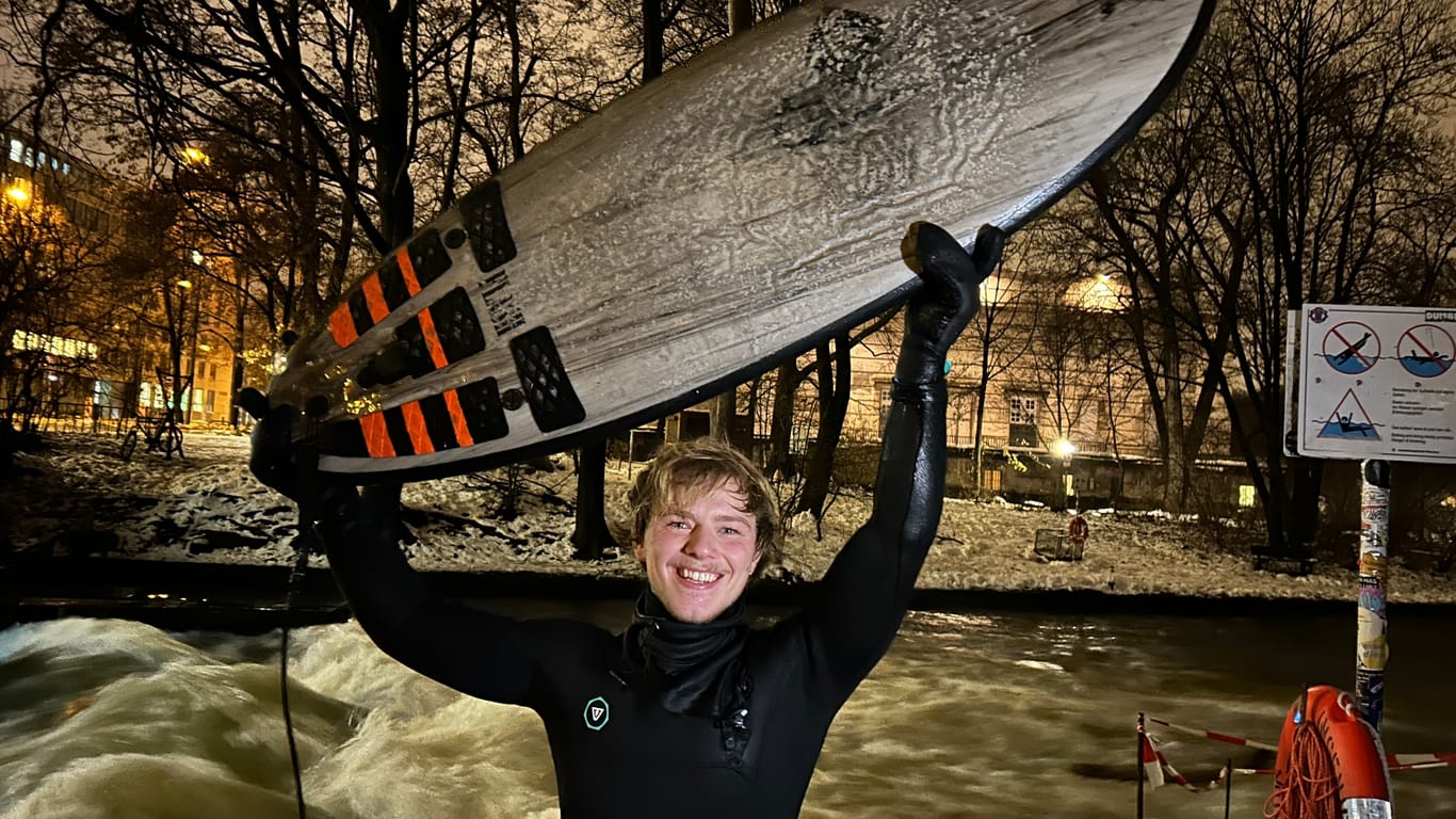 Johannes Mühlbauer mit seinem Surfbrett an der Eisbachwelle: Die Kälte macht ihm Dank seines Neoprenanzugs nichts aus.