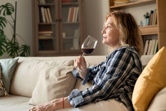 Eine Frau sitzt auf dem Sofa und trinkt ein Glas Wein.