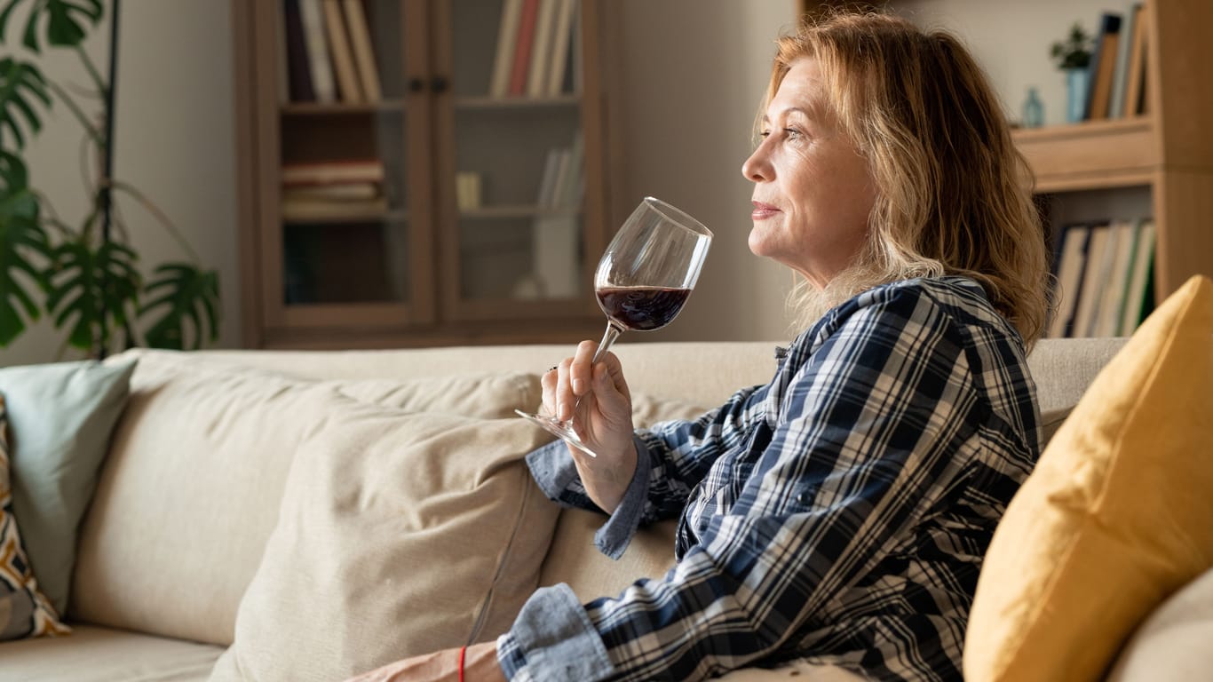 Eine Frau sitzt auf dem Sofa und trinkt ein Glas Wein.