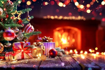 Geschenke liegen unter einem geschmückten Weihnachtsbaum, der vor einem brennenden Kaminfeuer steht