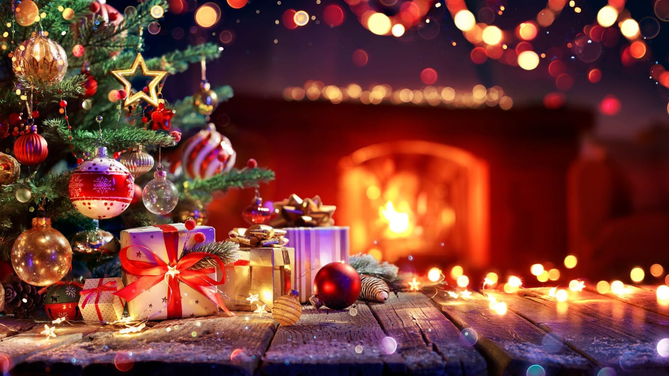 Geschenke liegen unter einem geschmückten Weihnachtsbaum, der vor einem brennenden Kaminfeuer steht