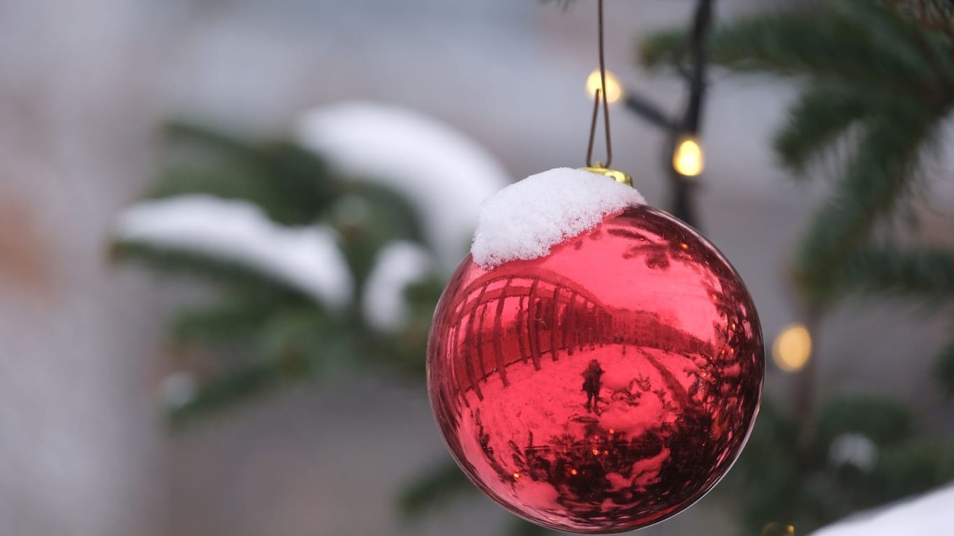 Rote Christbaumkugel mit Schnee (Symbolbild): Für viele Menschen sind weiße Weihnachten eine Idealvorstellung.
