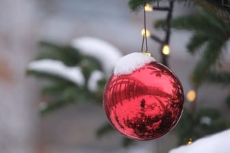 Rote Christbaumkugel mit Schnee (Symbolbild): Für viele Menschen sind weiße Weihnachten eine Idealvorstellung.