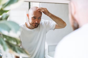 Ein Mann schaut in den Spiegel und befühlt seine Stirn