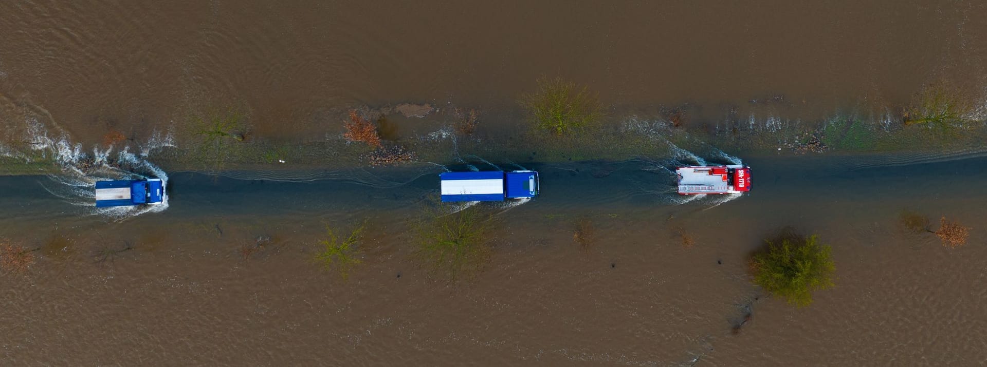 Ein Fahrzeug vom THW sowie der Feuerwehr fahren auf einer teilweise überfluteten Straße unweit der Aller (Aufnahme mit einer Drohne).