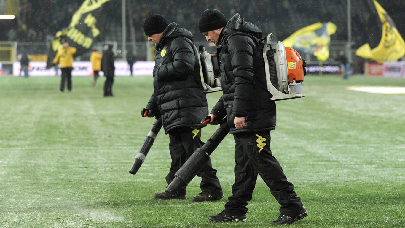 In Sportstadien im Winter ein vertrautes Bild (hier bei Borussia Dortmund in der Halbzeitpause): Helfer blasen die dünne Schneeschicht mit dem Laubbläser vom Rasen.
