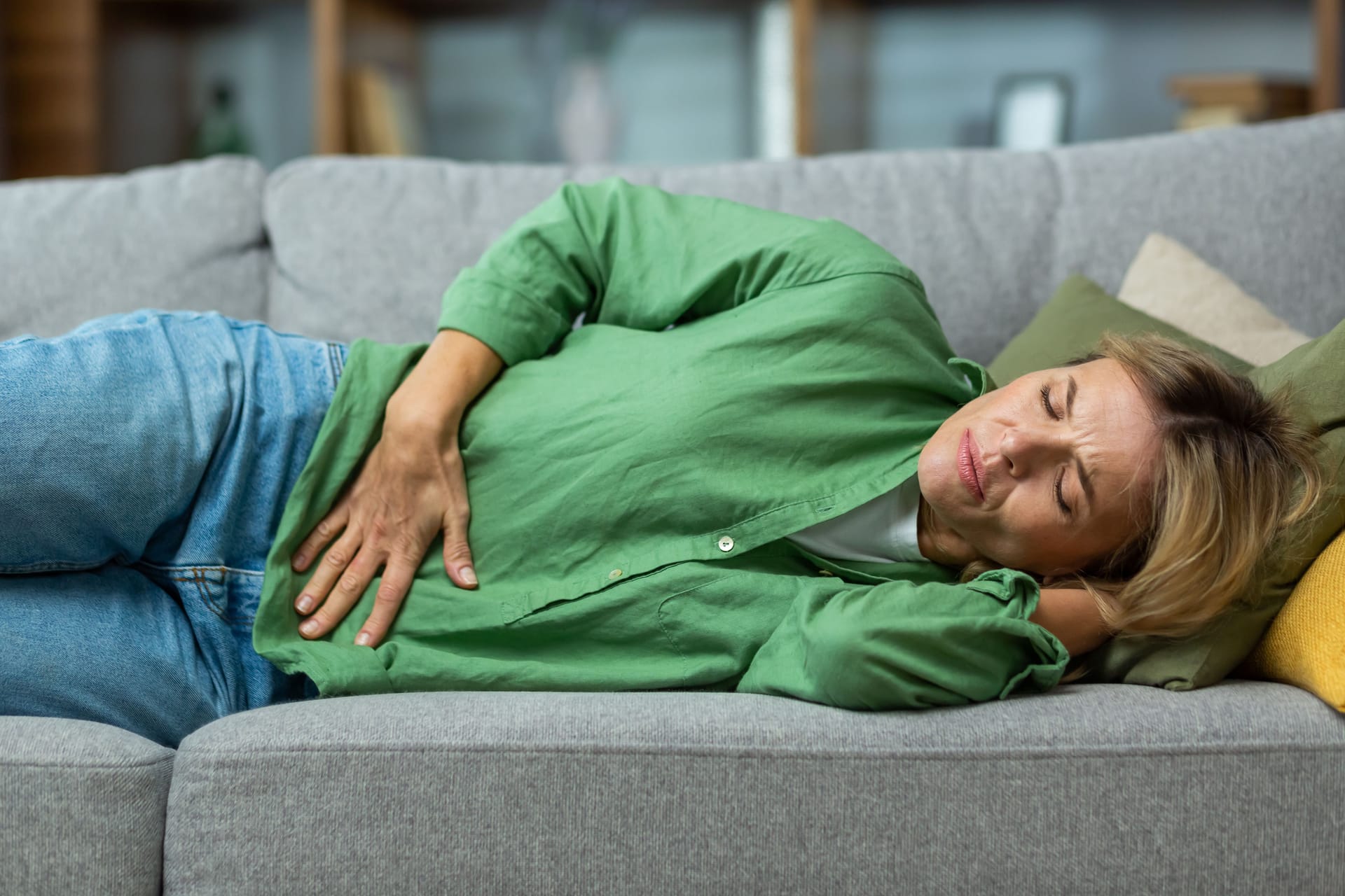 Frau liegt mit Bauchweh auf dem Sofa