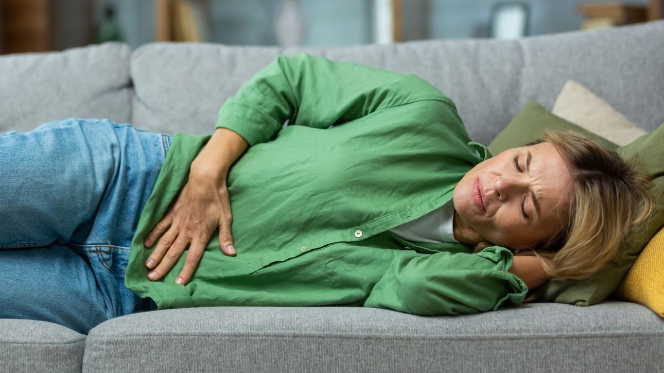 Frau liegt mit Bauchweh auf dem Sofa