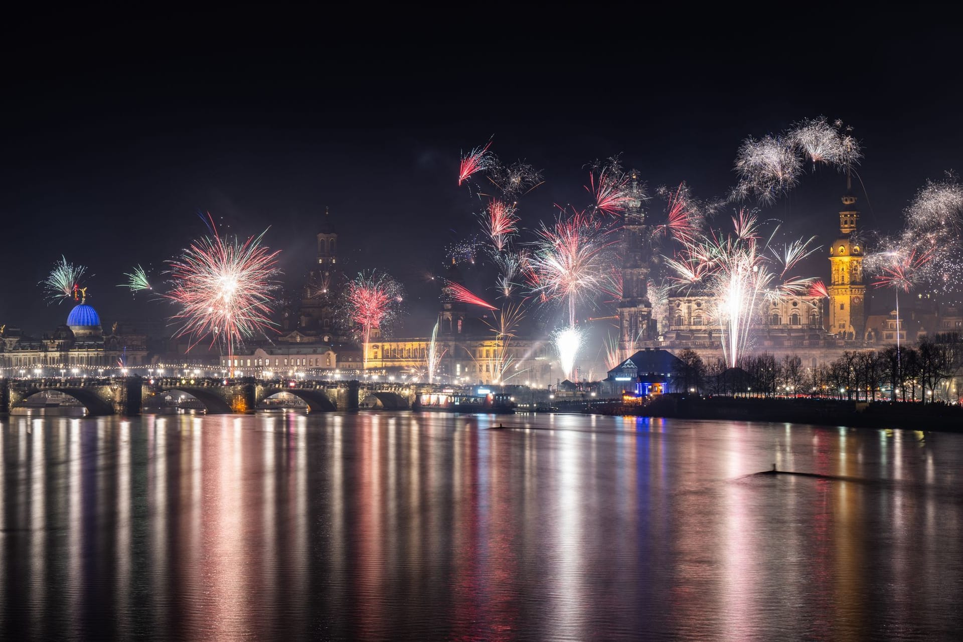 Feuerwerk explodiert in der Silvesternacht über der histoischen Altstadtkulisse an der Elbe: Zu sehen ist die Kuppel der Kunstakedmie mit dem Engel "Fama" (l-r), die Frauenkirche, das Ständehaus, die Hofkirche und der Hausmannsturm.