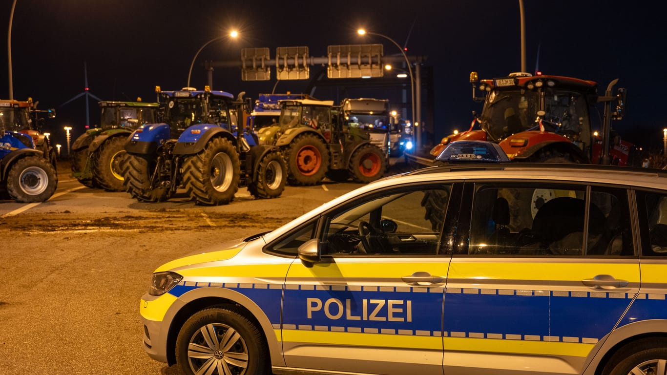 Ein Polizeifahrzeug steht vor einer Blockade mit Traktoren: Landwirte blockieren seit Montag eine Zufahrt der A7.