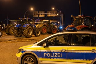 Ein Polizeifahrzeug steht vor einer Blockade mit Traktoren: Landwirte blockieren seit Montag eine Zufahrt der A7.