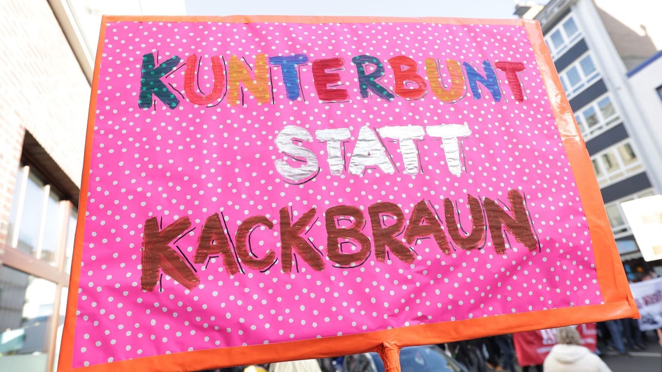"Kunterbunt statt kackbraun" steht auf einem rosa Plakat mit weißen Punkten, das auf einer Demonstration gegen rechts zu sehen.