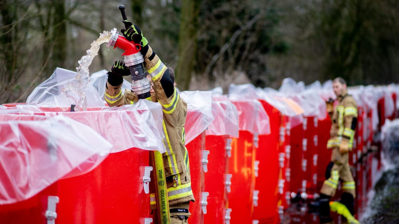 Einsatzkräfte der Feuerwehr befüllen ein mobiles Deichsystem, bestehend aus zahlreichen großen Behältern, mit Wasser. Der mobile Deich steht am Bümmersteder Fleth.