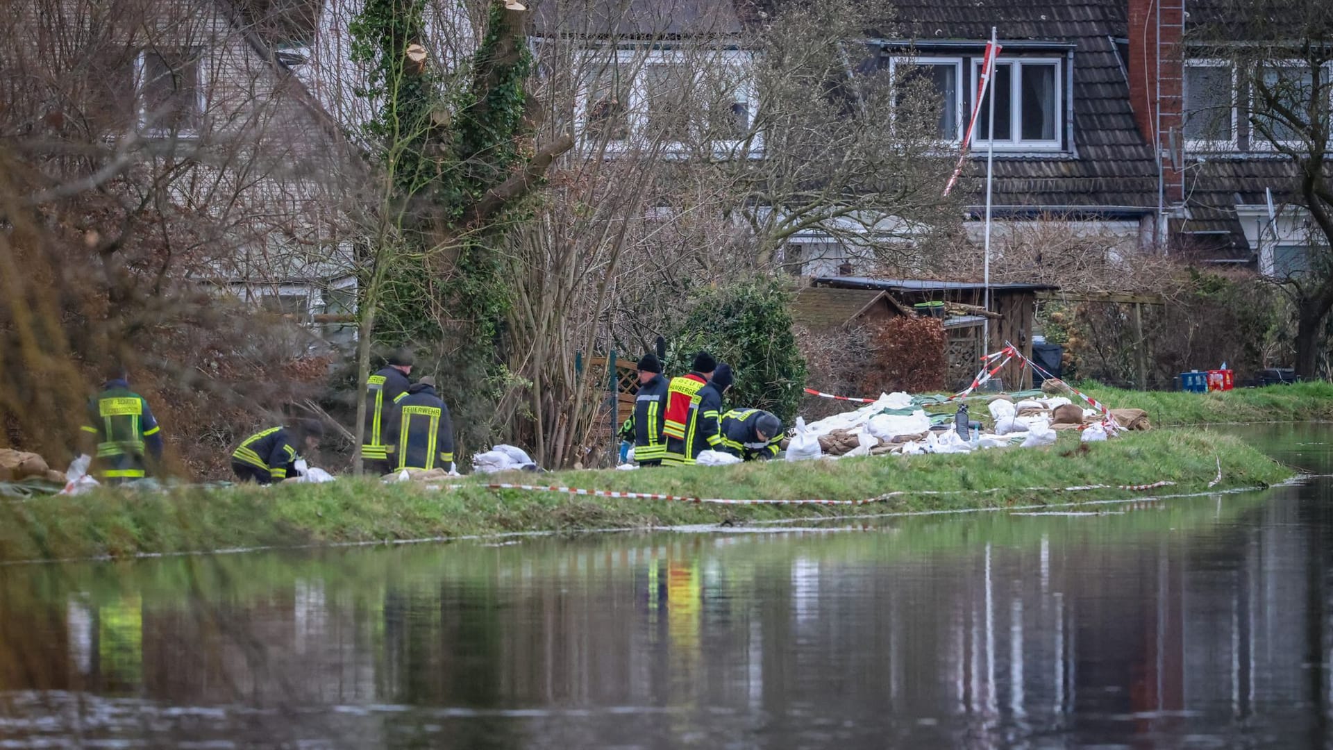 Helfer stehen neben Sandsäcken an einem Deich vor evakuierten Häusern an der Wörpe in Lilienthal. Da durch ein Deich zu brechen drohte, mussten Hunderte Bewohner ihre Häuser verlassen.