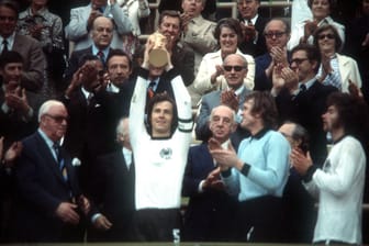 Kapitän Franz Beckenbauer reckt den WM-Pokal in die Höhe. Neben ihm (v.l.) seine Teamkollegen Sepp Maier und Paul Breitner.