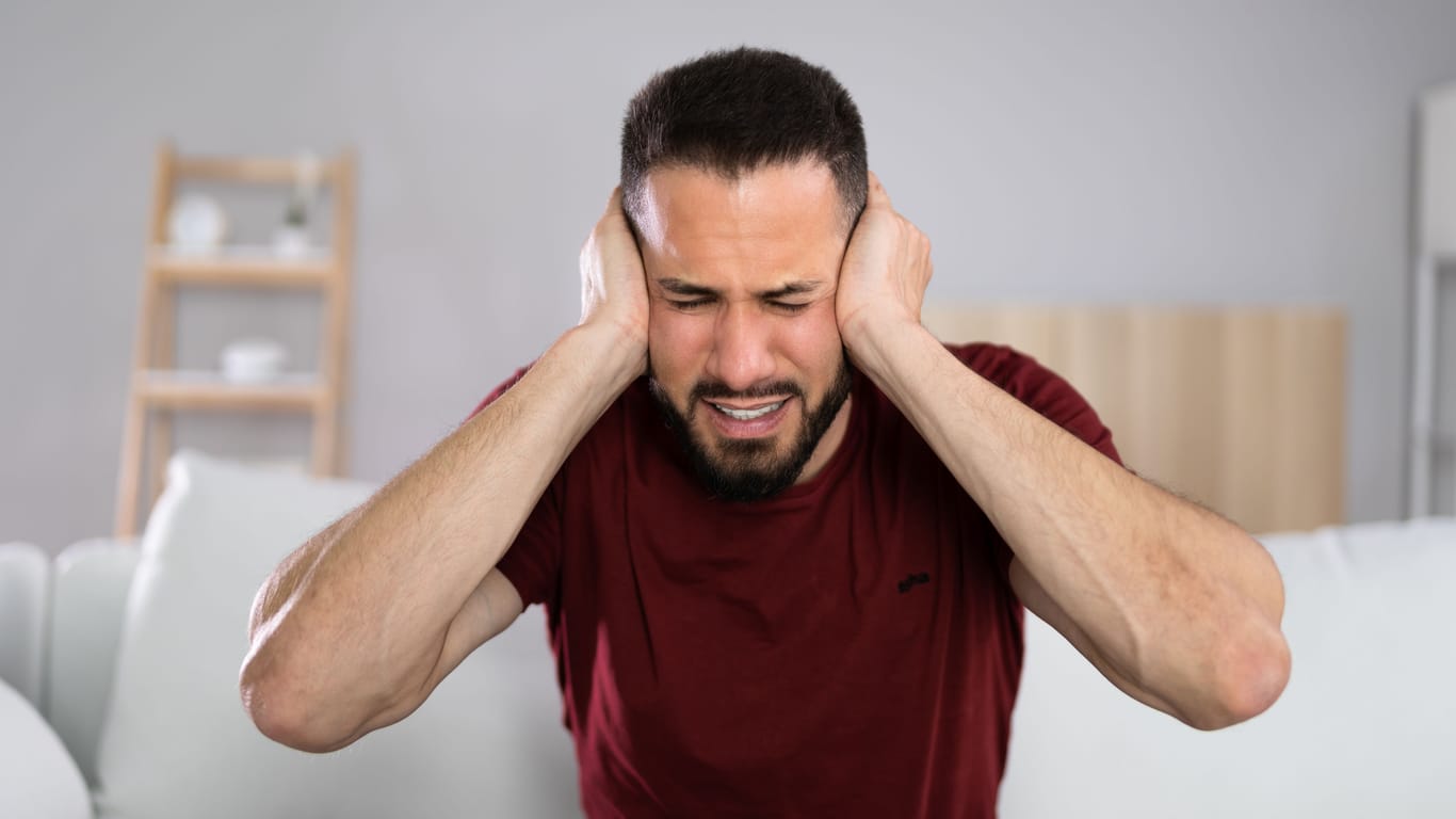 Ein Mann hält sich die Ohren zu: Wenn man Zuhause aufgrund einer ständigen Lärmbelästigung keine Erholung bekommt, wird es anstrengend.