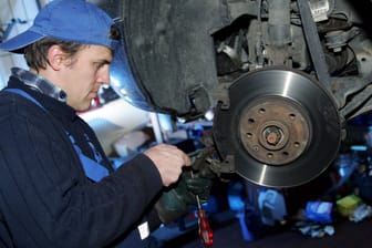 Ein Kfz-Mechaniker erneuert die Bremsbeläge an einem Pkw.