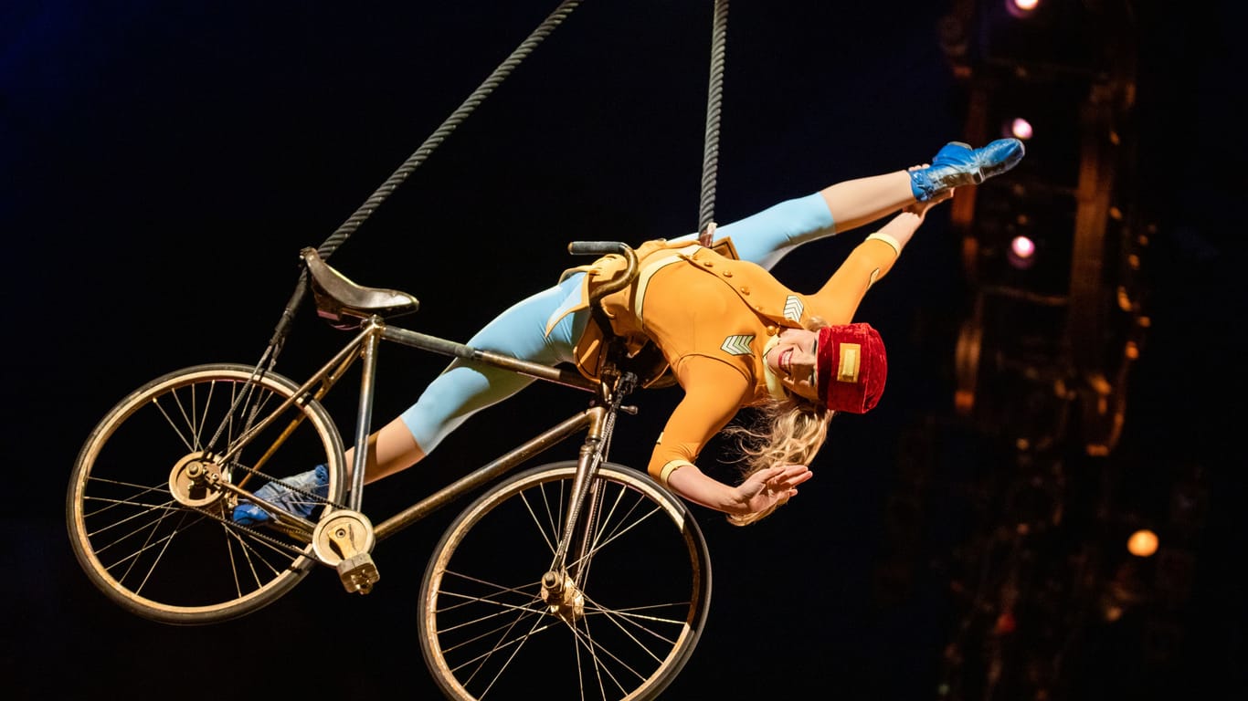Eine Artistin fliegt auf einem Fahrrad durch das Zirkuszelt.