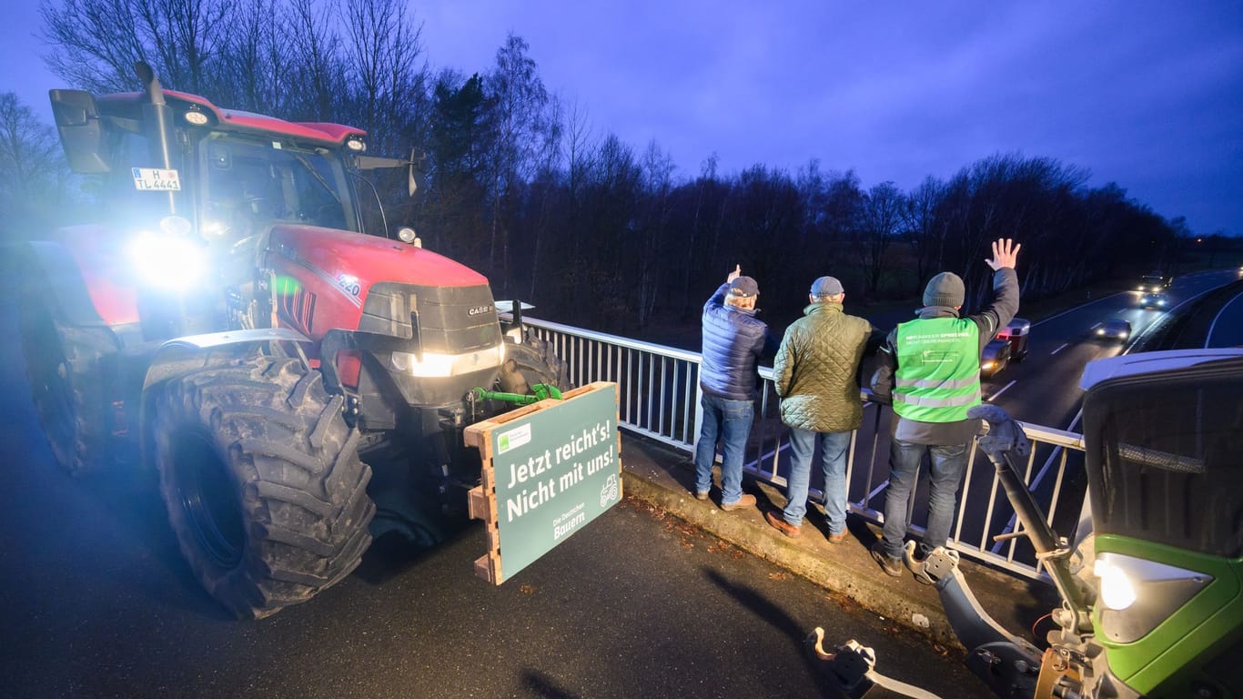 Landwirte stehen auf einer Brücke und winken Autofahrern zu. Insbesondere zur Mittagszeit sollen die Proteste auf viele Brücken sichtbar werden.