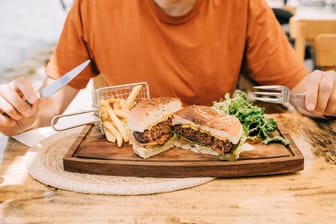 Ein Mann sitzt vor einem Burger-Menü (Symbolbild): Die schlechten Bewertungen stoßen dem Restaurant übel auf.