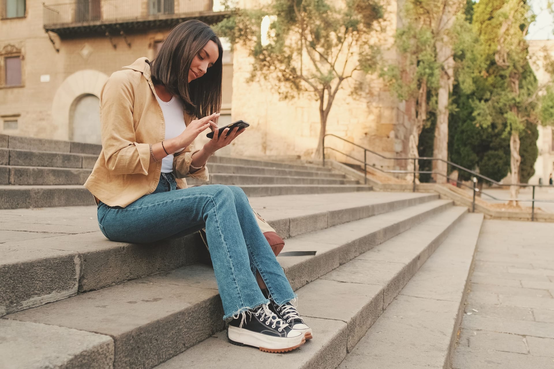 Traveler girl using looking mobile phone sitting on the steps of an old building in the historical part of an old European city