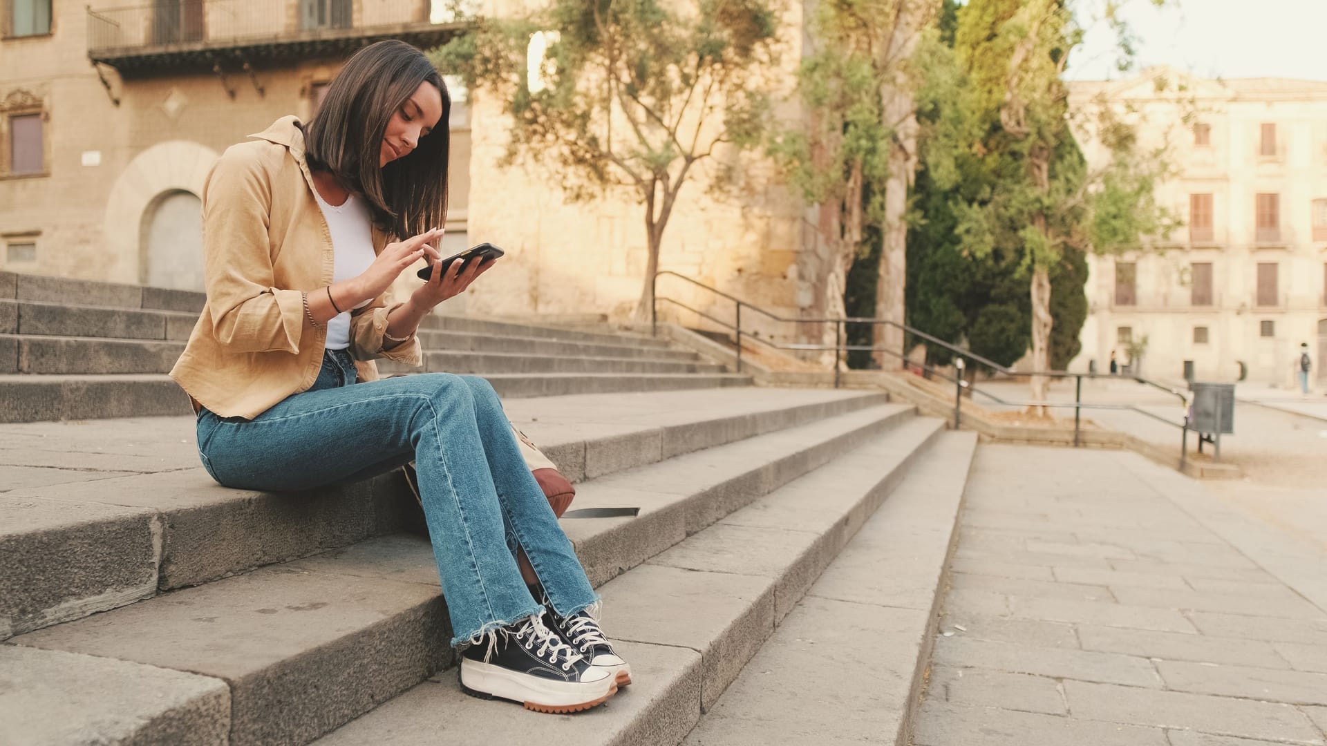 Traveler girl using looking mobile phone sitting on the steps of an old building in the historical part of an old European city