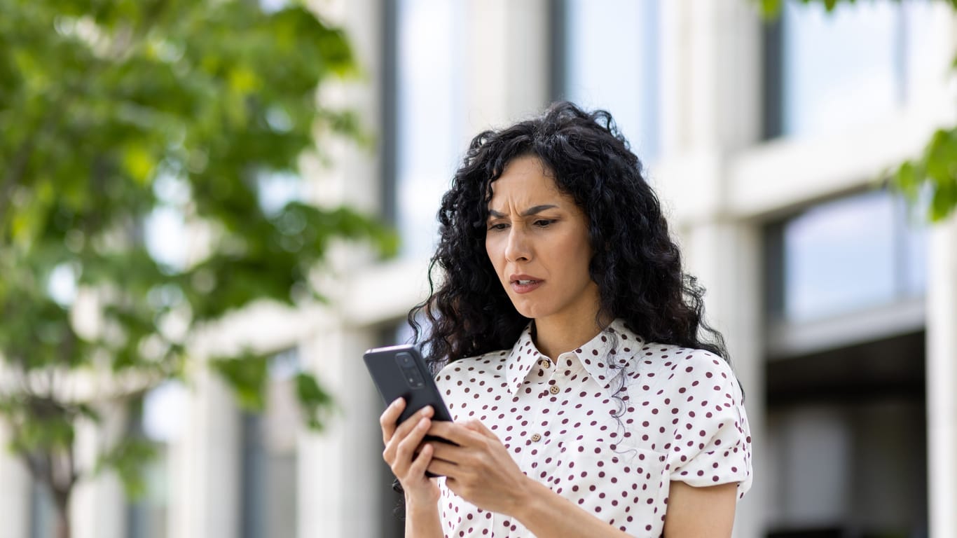 Sad disappointed woman received online notification with bad news on her phone, businesswoman walking outside office building, using application on smartphone, reading social media unsatisfied