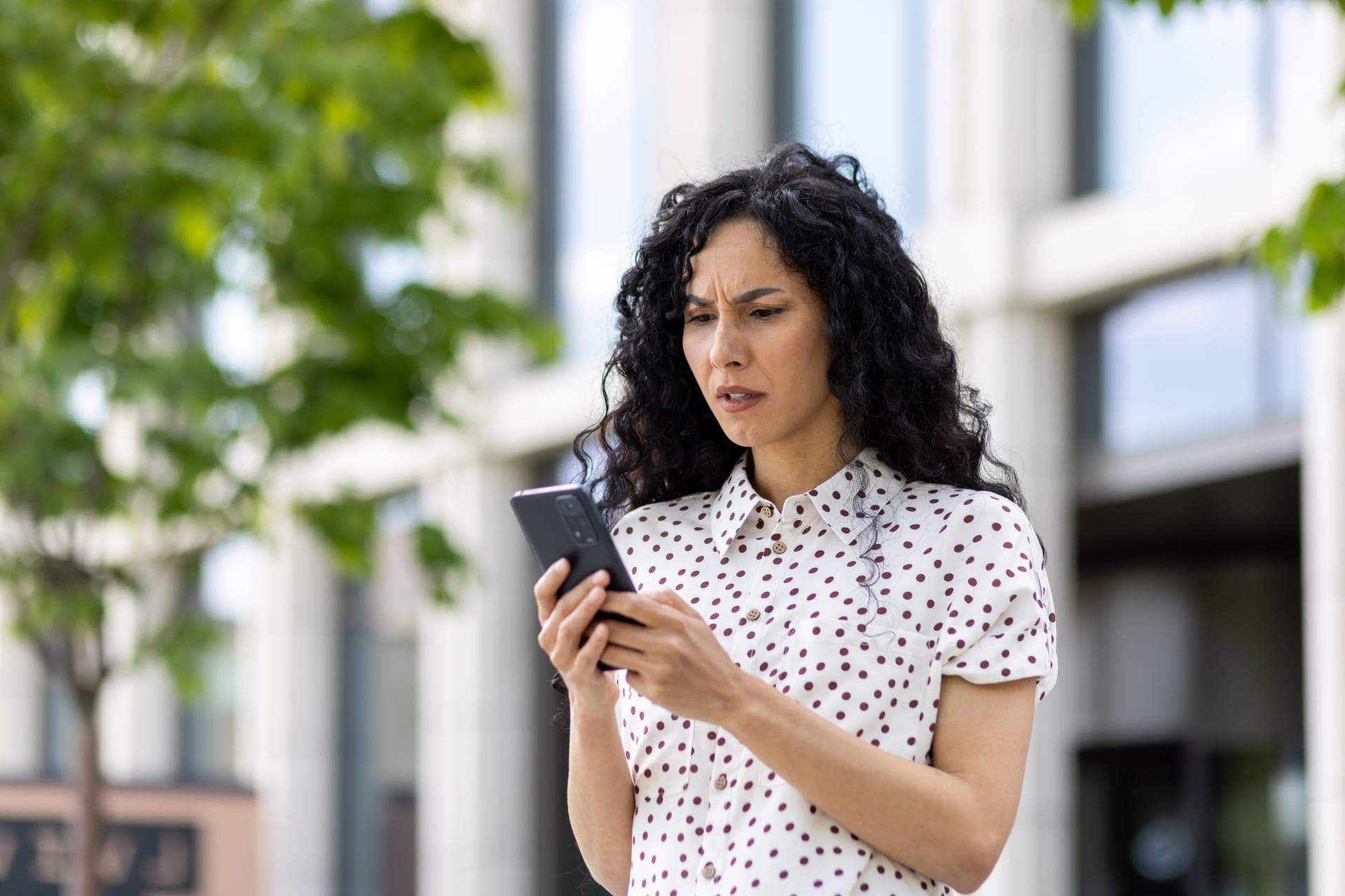 Sad disappointed woman received online notification with bad news on her phone, businesswoman walking outside office building, using application on smartphone, reading social media unsatisfied