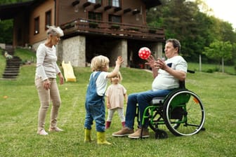 Mann im Rollstuhl spielt mit den Kindern Ball