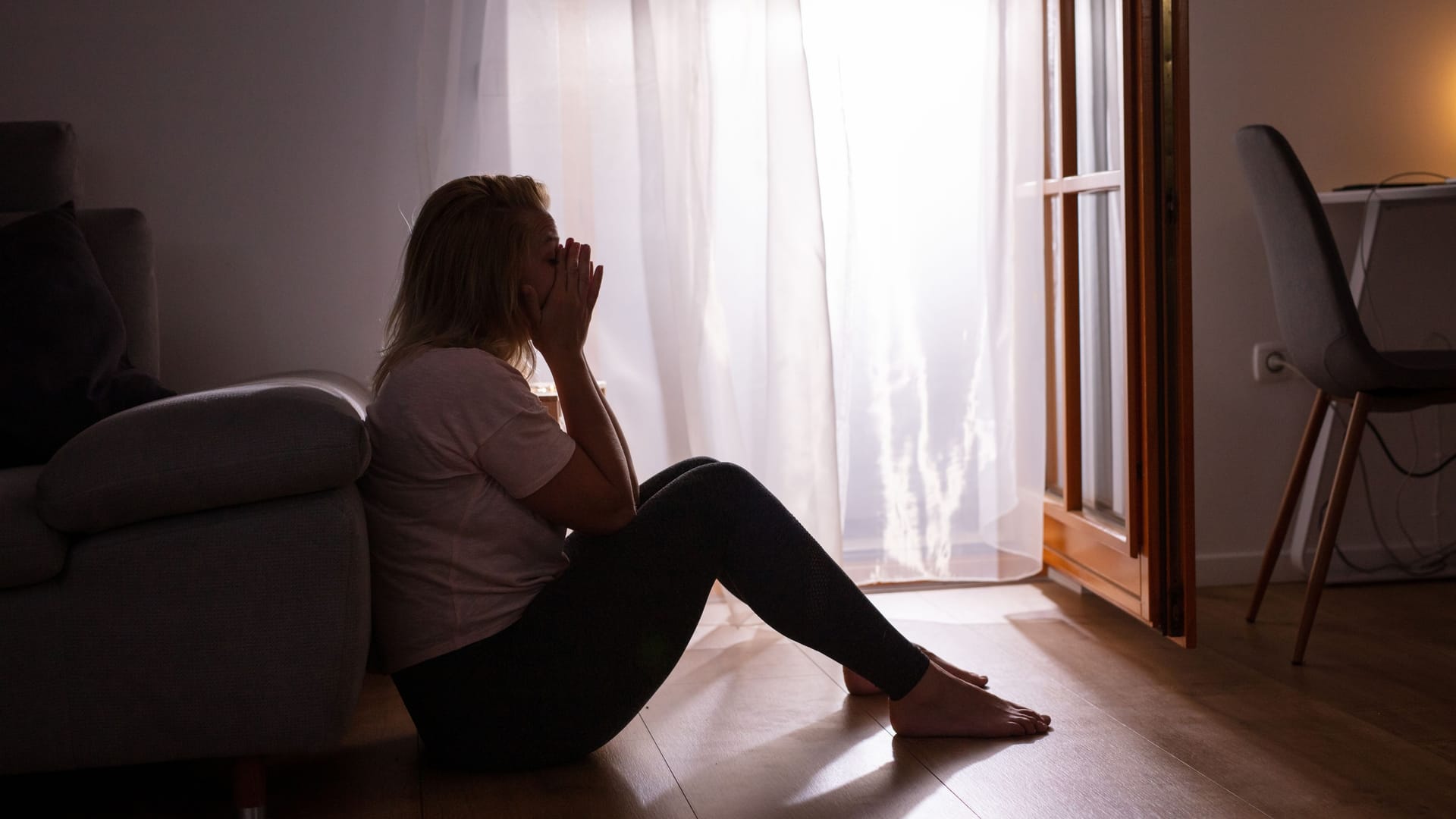 Eine Frau sitzt niedergeschlagen am Fenster