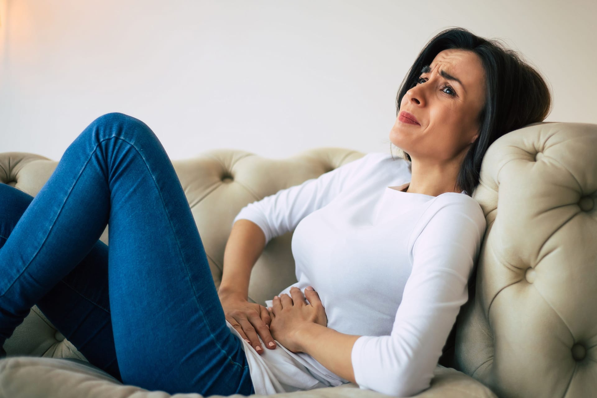 Frau sitzt mit Bauchweh auf dem Sofa