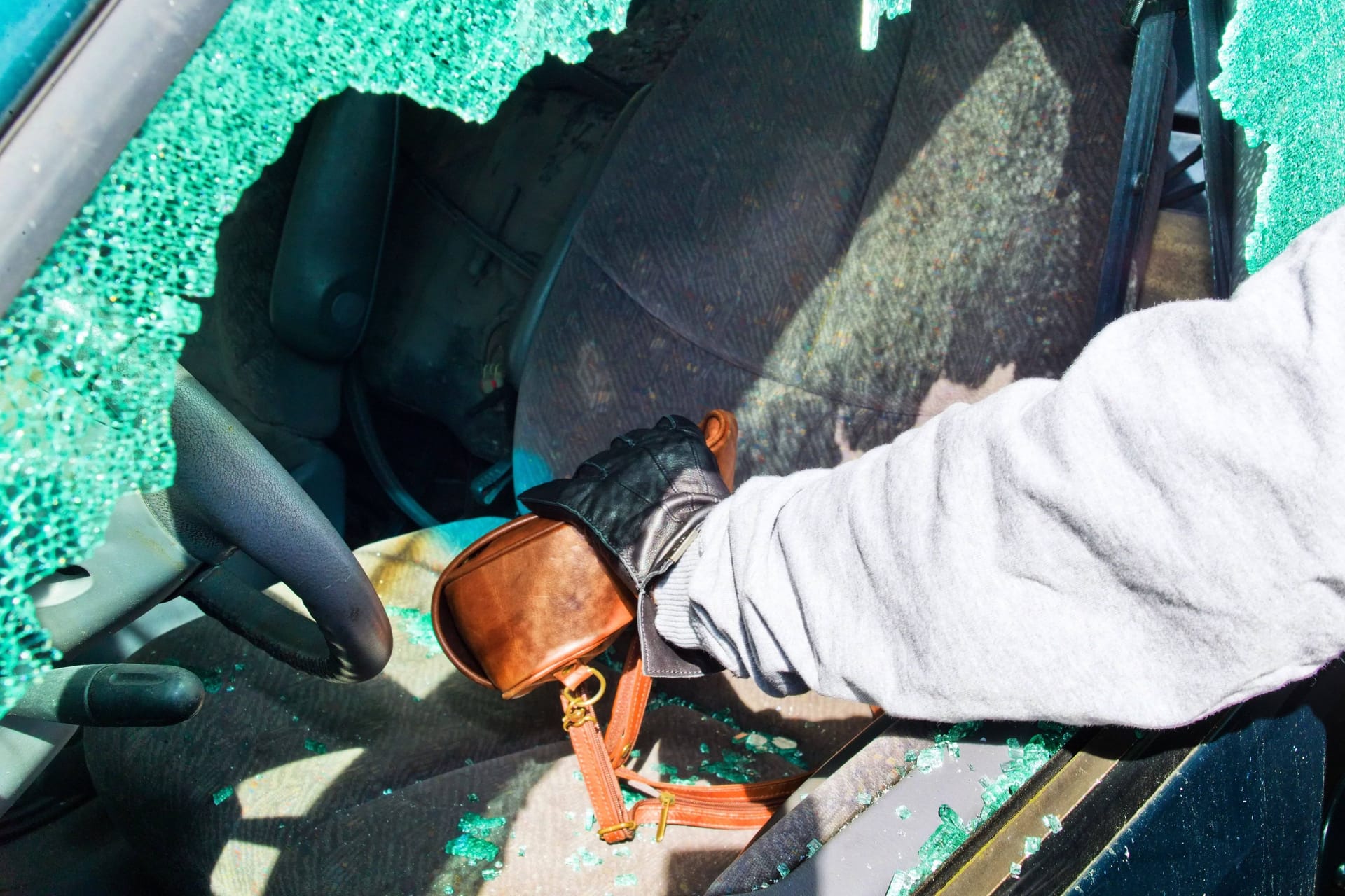 Ein Dieb stiehlt eine Handtasche aus einem Auto (Symbolbild): Im Landkreis Hameln-Pyrmont sind mehrere Autos aufgebrochen worden.